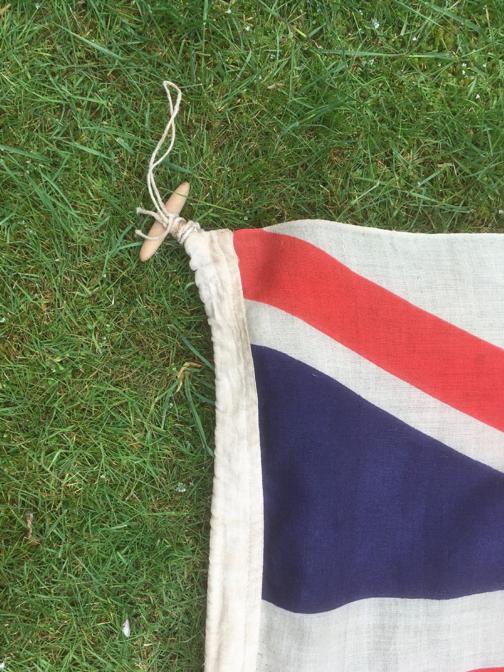 A rectangular Second World War Royal Navy White Ensign flag featuring a white field with a red Saint Georges Cross, a Union Jack canton, and a stitched canvas edge with rope lanyard. View XII