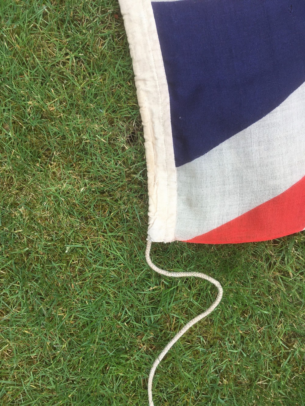 A rectangular Second World War Royal Navy White Ensign flag featuring a white field with a red Saint Georges Cross, a Union Jack canton, and a stitched canvas edge with rope lanyard. View XIII