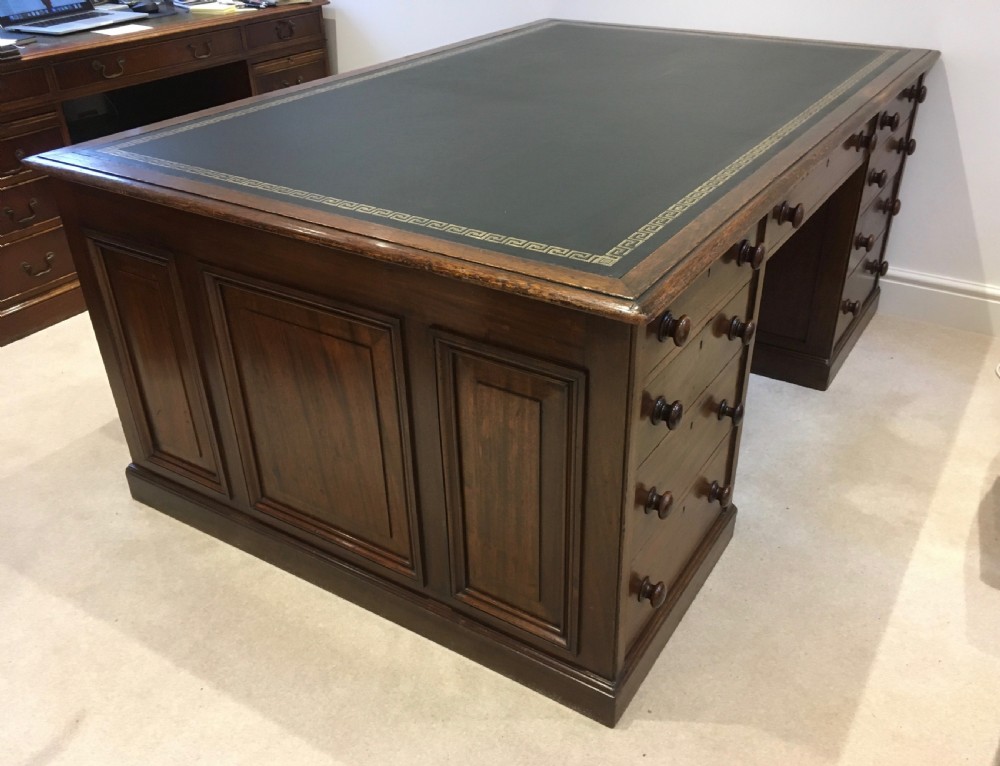 A large mahogany partners desk featuring a dark green gold-tooled leather writing surface and twin pedestals with turned knob handles.