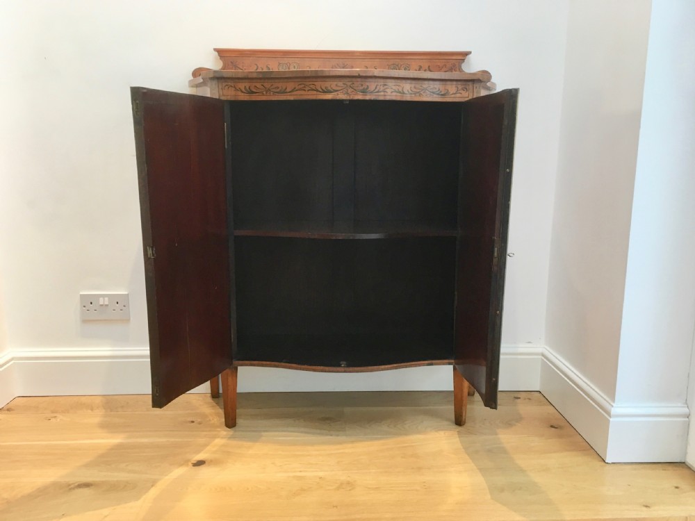 A satinwood side cabinet featuring a serpentine front, twin cupboard doors decorated with hand-painted Neoclassical urns and floral swags, supported by tapered legs. View VIII