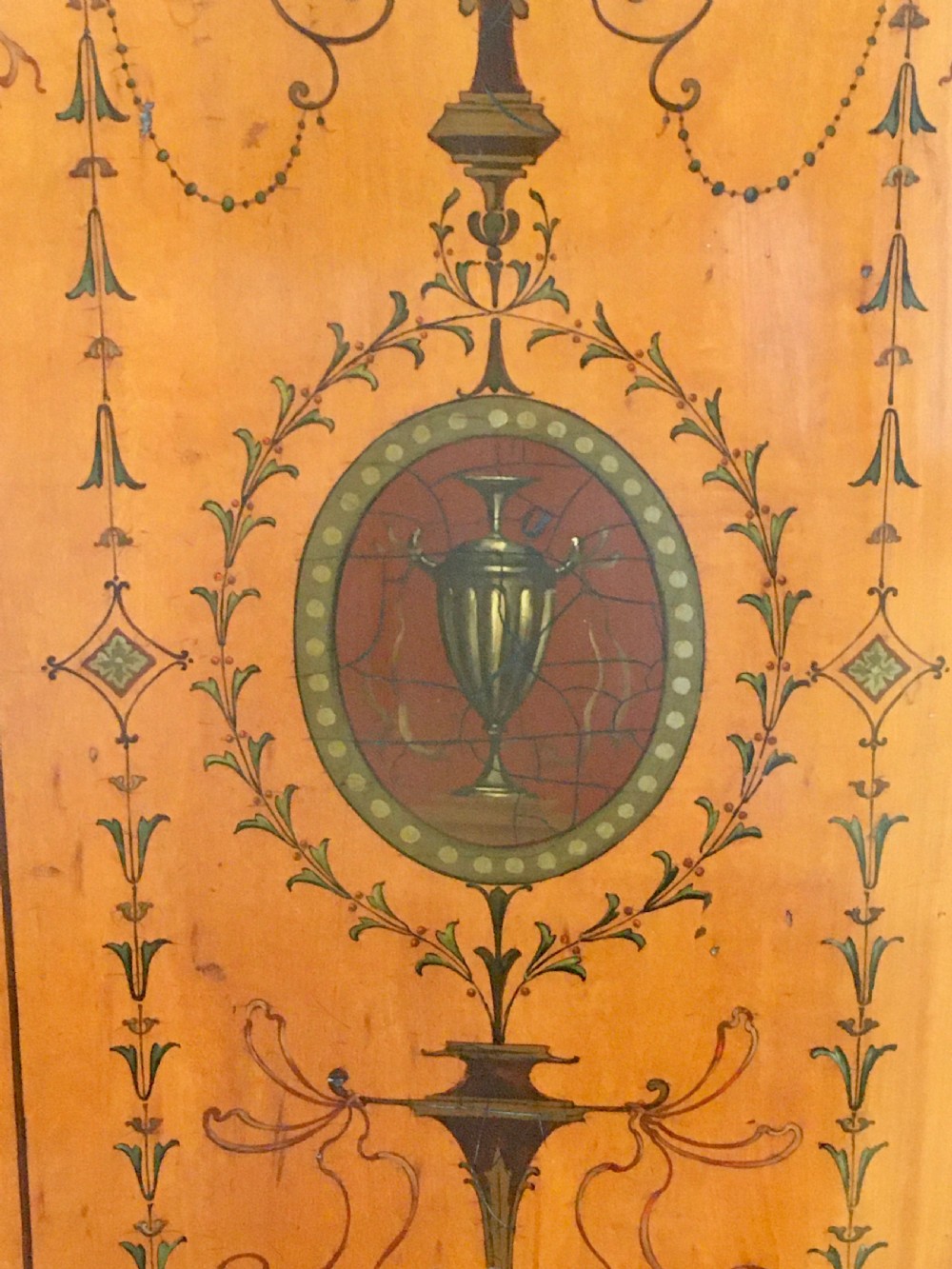 A satinwood side cabinet featuring a serpentine front, twin cupboard doors decorated with hand-painted Neoclassical urns and floral swags, supported by tapered legs. View IX