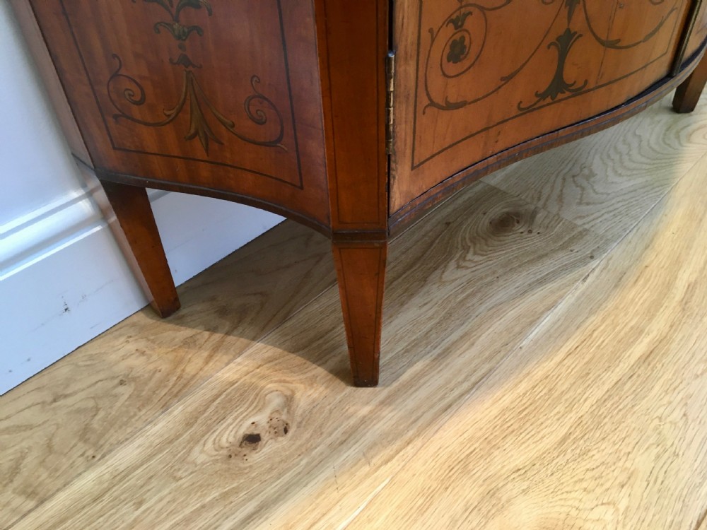 A satinwood side cabinet featuring a serpentine front, twin cupboard doors decorated with hand-painted Neoclassical urns and floral swags, supported by tapered legs. View XVI