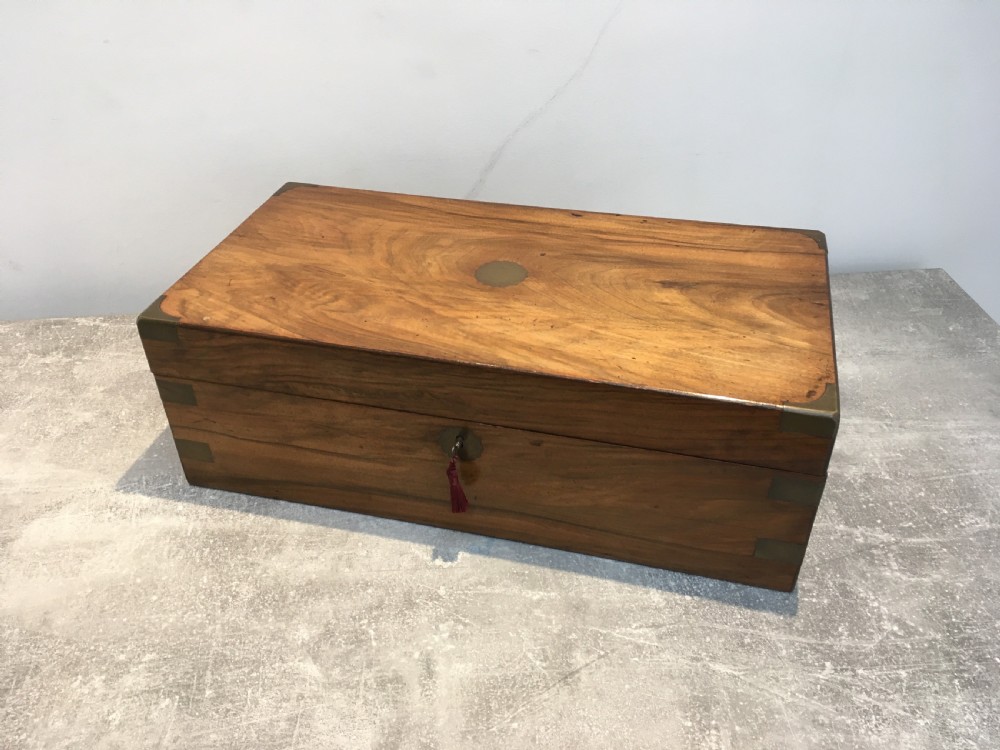 A rectangular Georgian walnut writing slope featuring brass corner brackets, a central round brass medallion, and a front key escutcheon with a red tassel.