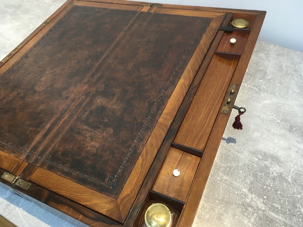 A rectangular Georgian walnut writing slope featuring brass corner brackets, a central round brass medallion, and a front key escutcheon with a red tassel. View V