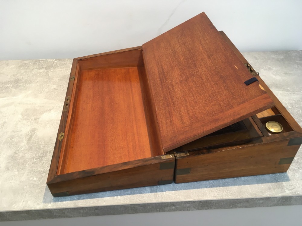 A rectangular Georgian walnut writing slope featuring brass corner brackets, a central round brass medallion, and a front key escutcheon with a red tassel. View VI