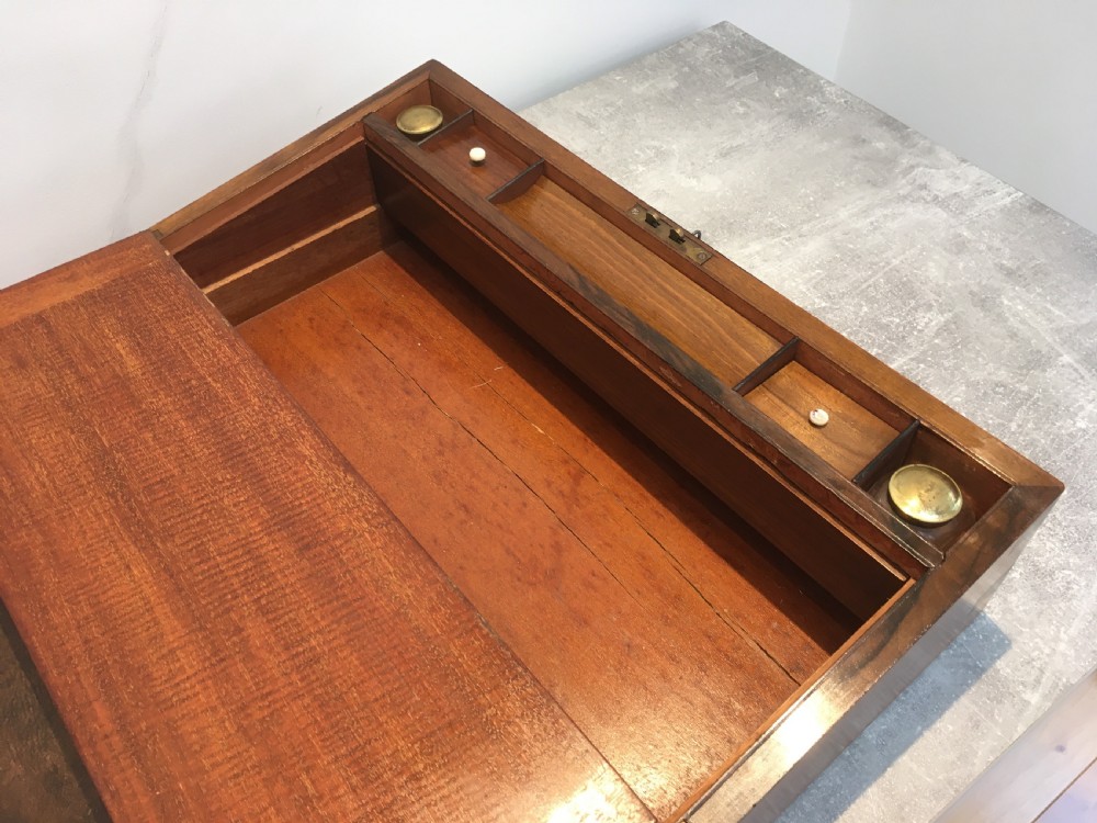 A rectangular Georgian walnut writing slope featuring brass corner brackets, a central round brass medallion, and a front key escutcheon with a red tassel. View VIII