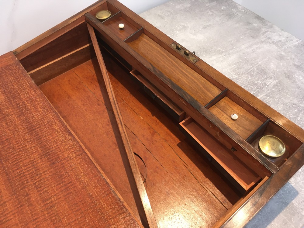 A rectangular Georgian walnut writing slope featuring brass corner brackets, a central round brass medallion, and a front key escutcheon with a red tassel. View IX