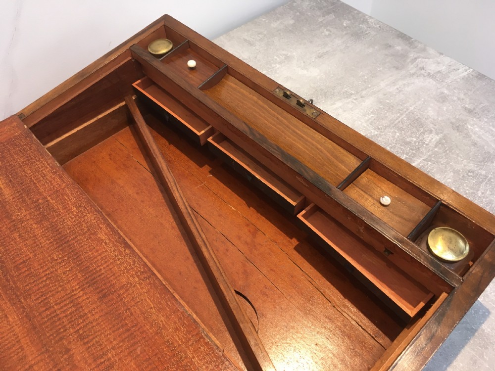 A rectangular Georgian walnut writing slope featuring brass corner brackets, a central round brass medallion, and a front key escutcheon with a red tassel. View X