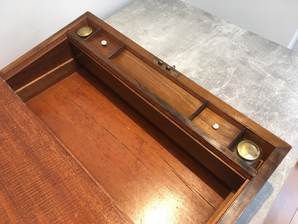 A rectangular Georgian walnut writing slope featuring brass corner brackets, a central round brass medallion, and a front key escutcheon with a red tassel. View XI