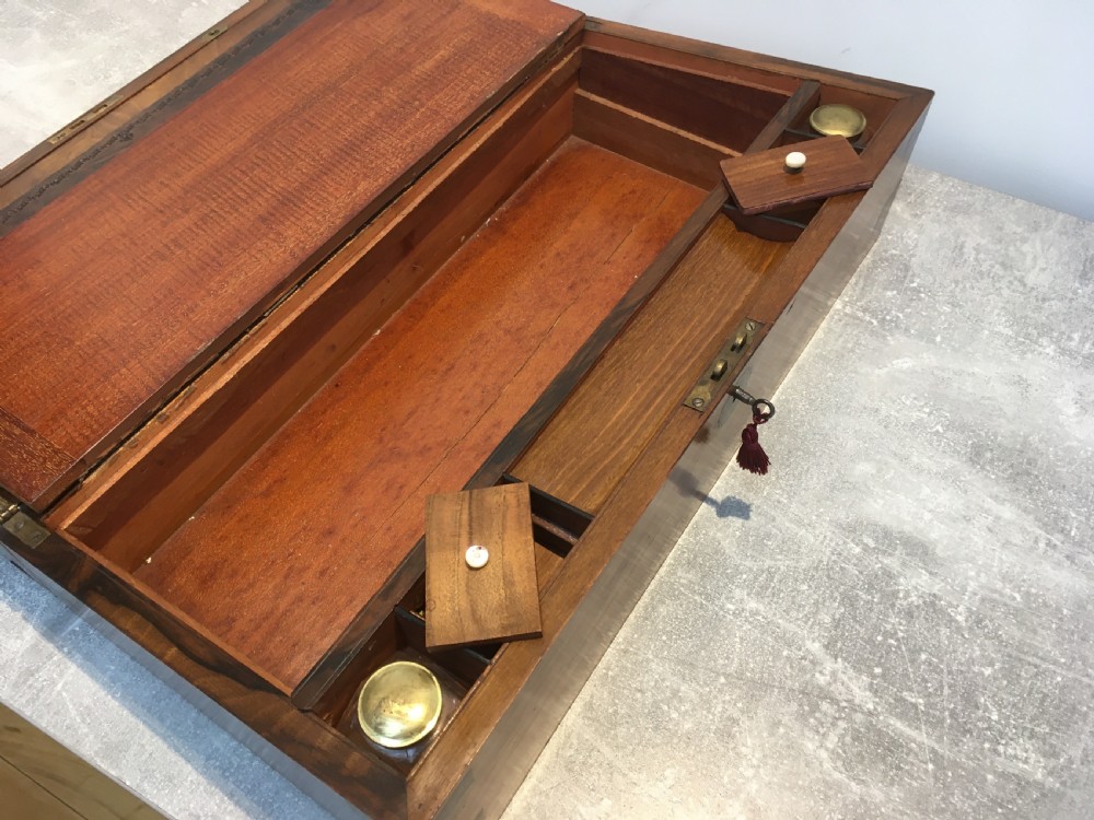 A rectangular Georgian walnut writing slope featuring brass corner brackets, a central round brass medallion, and a front key escutcheon with a red tassel. View XII