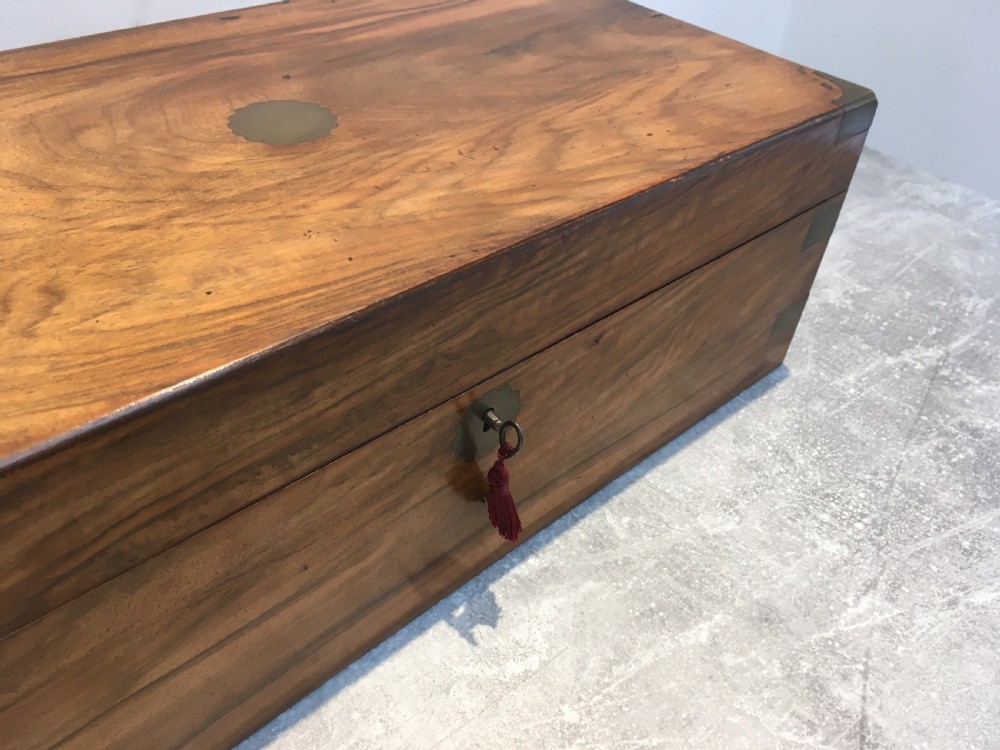 A rectangular Georgian walnut writing slope featuring brass corner brackets, a central round brass medallion, and a front key escutcheon with a red tassel. View XV