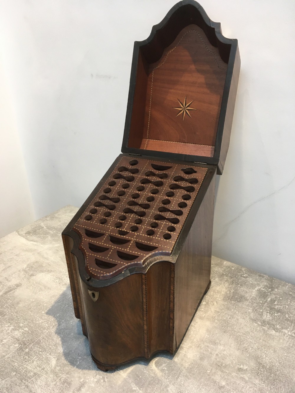 A George III mahogany slanted-top knife box shown open, featuring slotted interior fittings, string inlay, and a star marquetry motif on the inside lid.