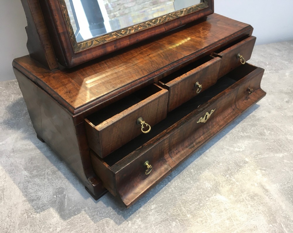 An 18th-century walnut toilet mirror featuring an adjustable rectangular glass frame set above a stepped base with small drawers and brass drop handles. View VI