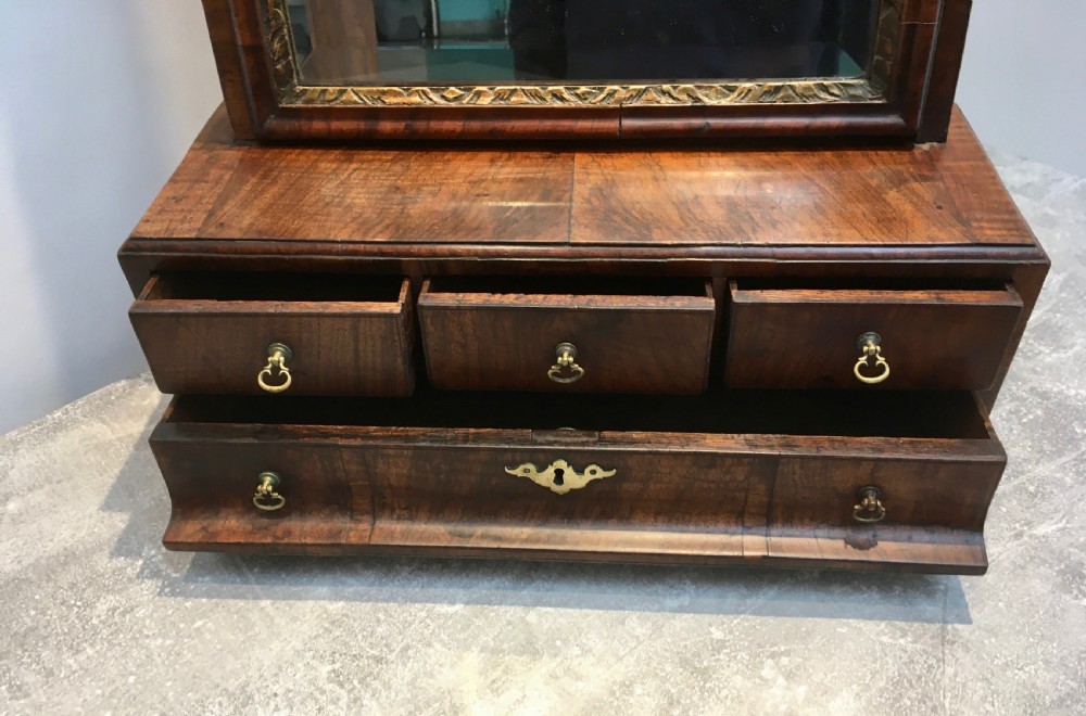 An 18th-century walnut toilet mirror featuring an adjustable rectangular glass frame set above a stepped base with small drawers and brass drop handles. View VII