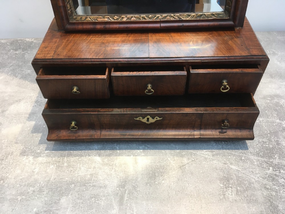 An 18th-century walnut toilet mirror featuring an adjustable rectangular glass frame set above a stepped base with small drawers and brass drop handles. View XIV