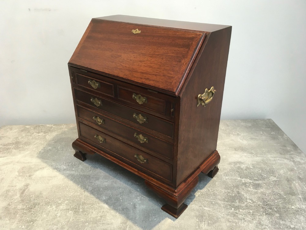 A miniature dark mahogany fall front bureau featuring tiered drawers, side carrying handles, brass hardware, and ogee bracket feet. View III