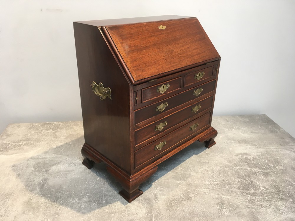 A miniature dark mahogany fall front bureau featuring tiered drawers, side carrying handles, brass hardware, and ogee bracket feet. View IV
