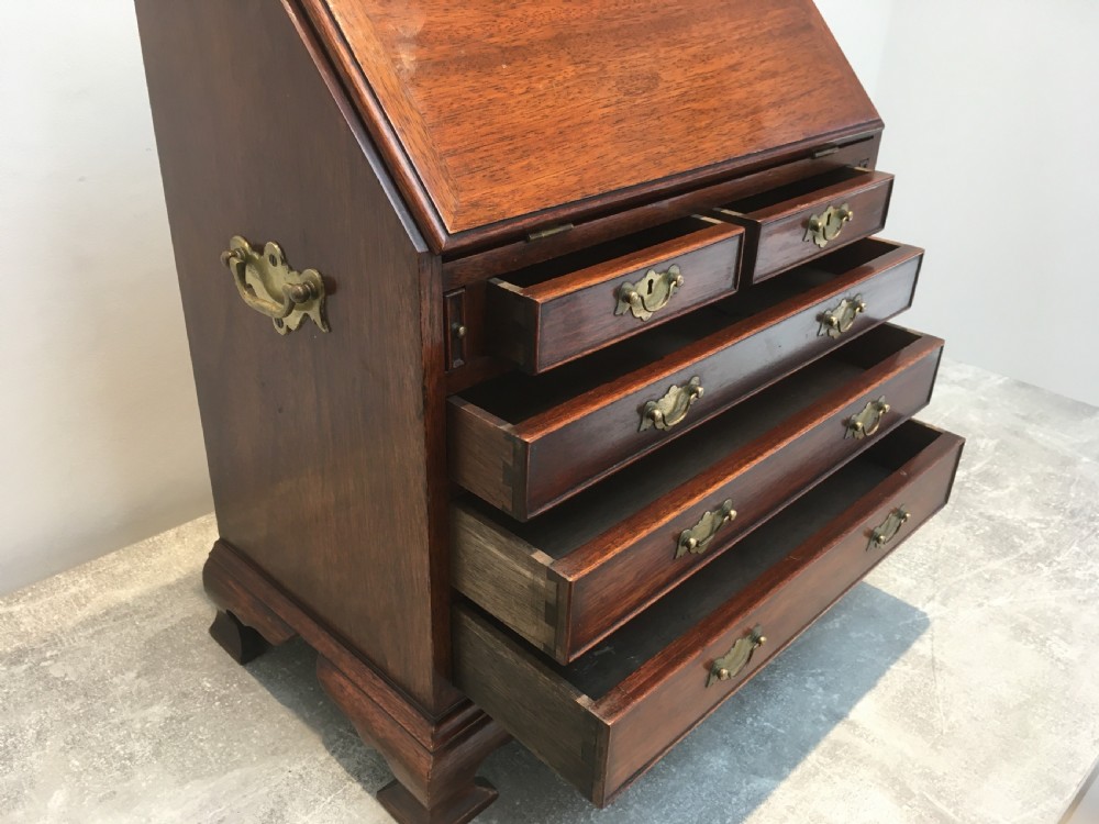 A miniature dark mahogany fall front bureau featuring tiered drawers, side carrying handles, brass hardware, and ogee bracket feet. View VII