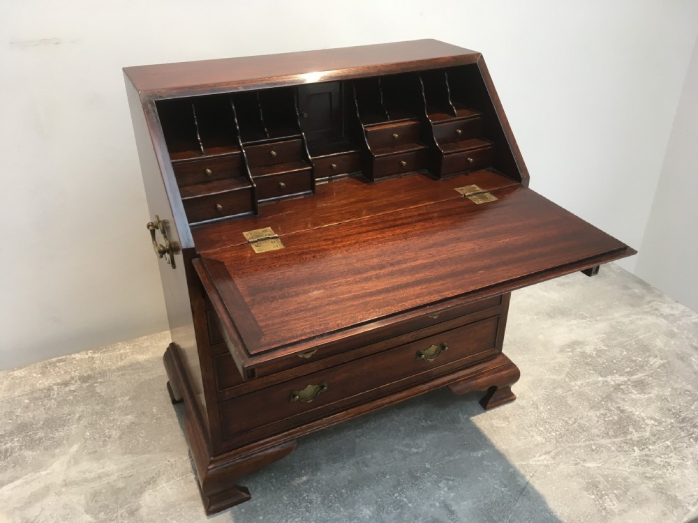 A miniature dark mahogany fall front bureau featuring tiered drawers, side carrying handles, brass hardware, and ogee bracket feet. View VIII