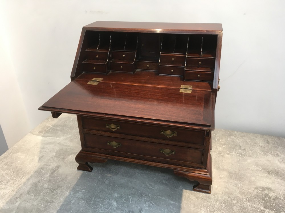 A miniature dark mahogany fall front bureau featuring tiered drawers, side carrying handles, brass hardware, and ogee bracket feet. View IX