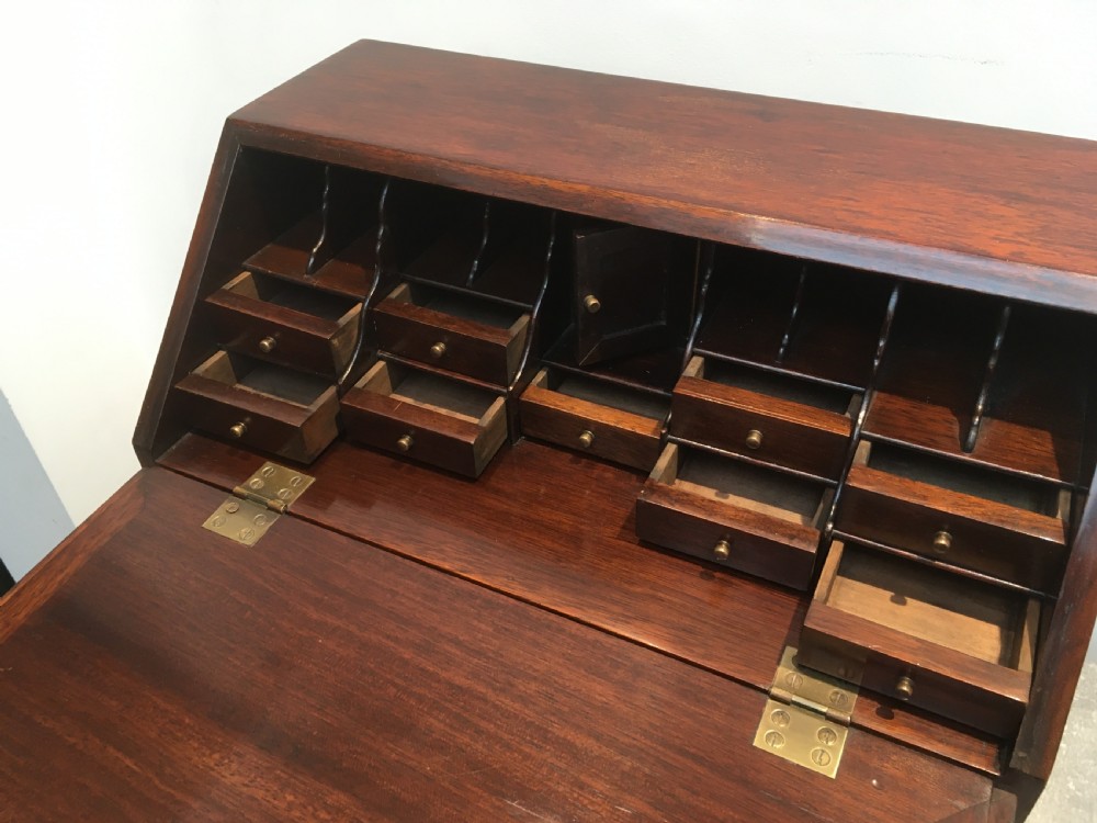 A miniature dark mahogany fall front bureau featuring tiered drawers, side carrying handles, brass hardware, and ogee bracket feet. View X