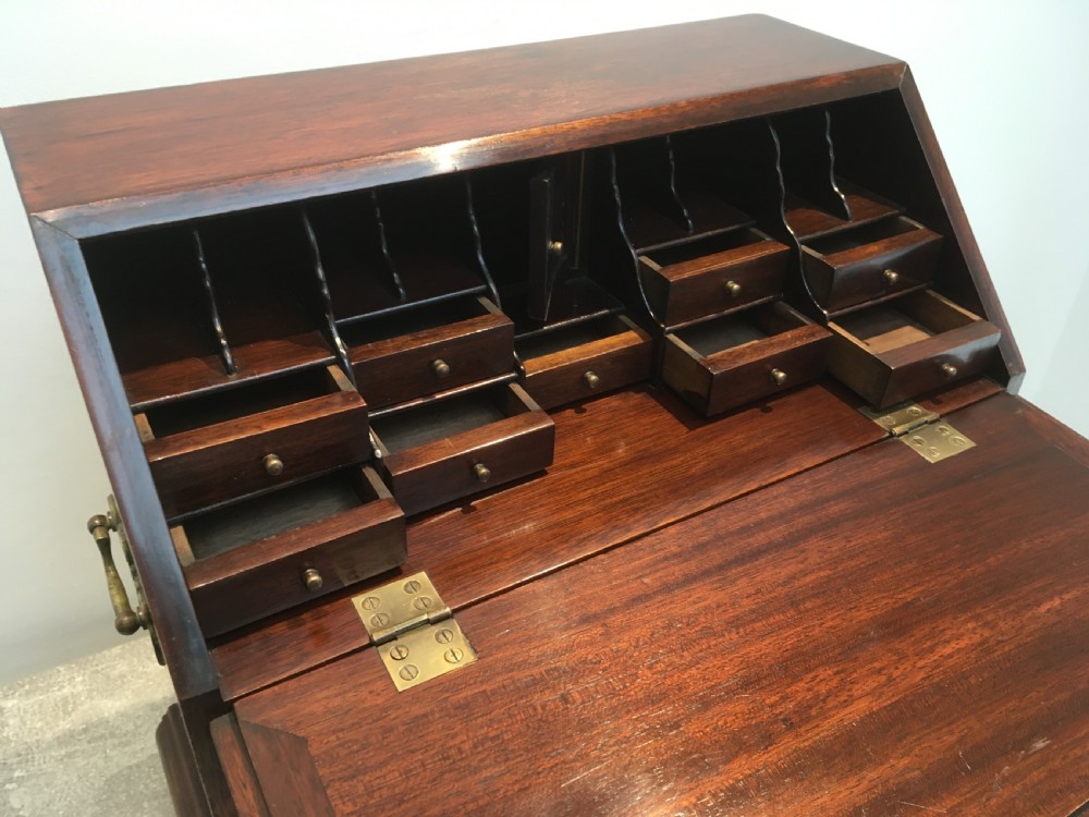A miniature dark mahogany fall front bureau featuring tiered drawers, side carrying handles, brass hardware, and ogee bracket feet. View XI