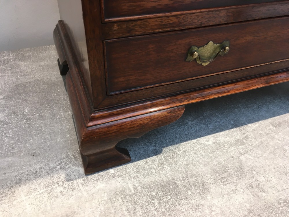 A miniature dark mahogany fall front bureau featuring tiered drawers, side carrying handles, brass hardware, and ogee bracket feet. View XII