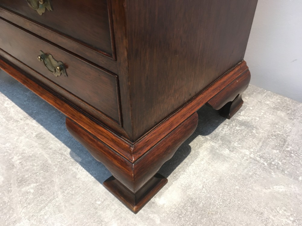 A miniature dark mahogany fall front bureau featuring tiered drawers, side carrying handles, brass hardware, and ogee bracket feet. View XIII