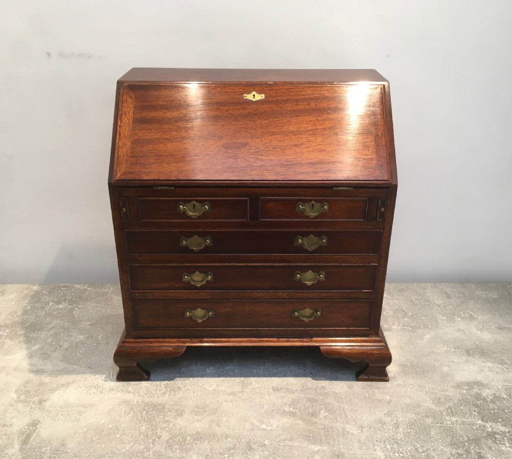 A miniature dark mahogany fall front bureau featuring tiered drawers, side carrying handles, brass hardware, and ogee bracket feet. View XV