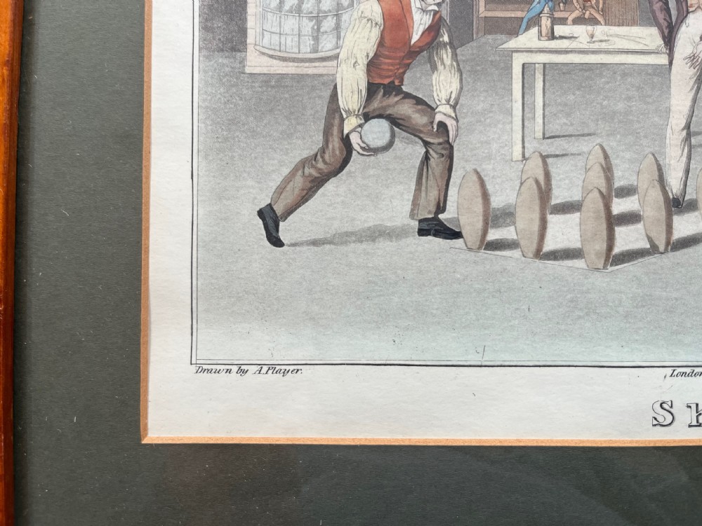 A framed antique hand-coloured engraving depicting gentlemen playing skittles outside an English pub, set within a dark green mount and a warm wood frame. View V