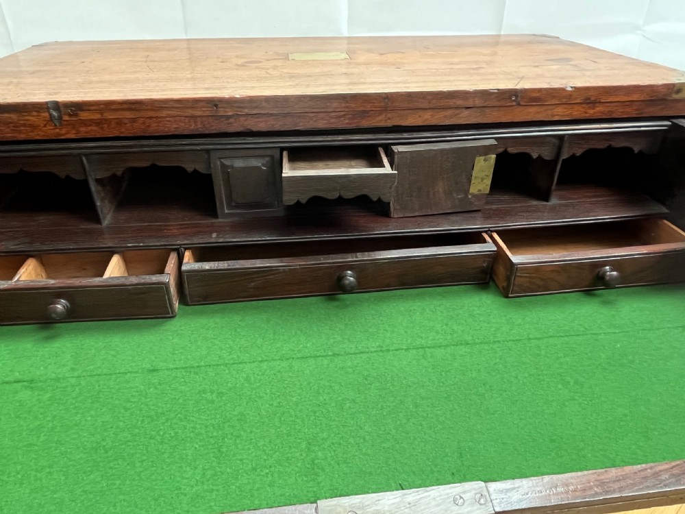 A teak campaign secretaire chest featuring brass corner brackets, flush brass drawer handles, and an open fall-front writing surface lined with green felt. View V