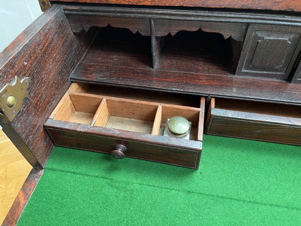 A teak campaign secretaire chest featuring brass corner brackets, flush brass drawer handles, and an open fall-front writing surface lined with green felt. View VIII