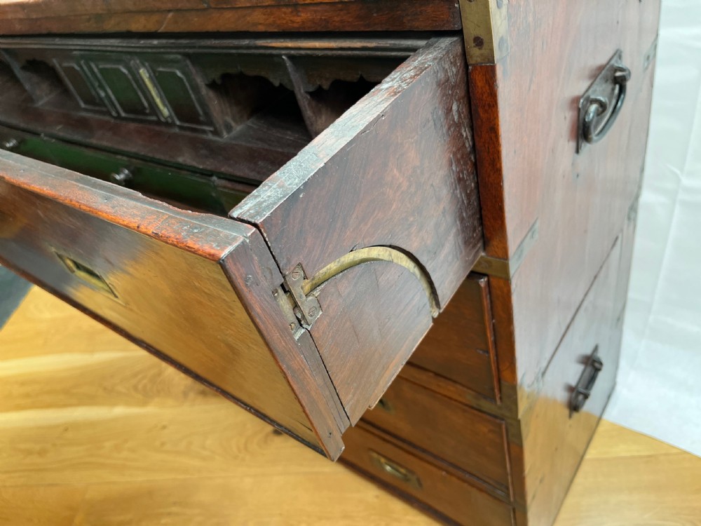 A teak campaign secretaire chest featuring brass corner brackets, flush brass drawer handles, and an open fall-front writing surface lined with green felt. View IX