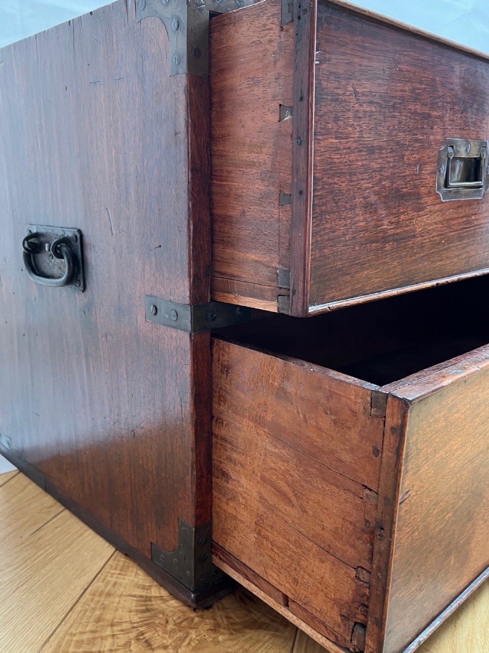 A teak campaign secretaire chest featuring brass corner brackets, flush brass drawer handles, and an open fall-front writing surface lined with green felt. View XV