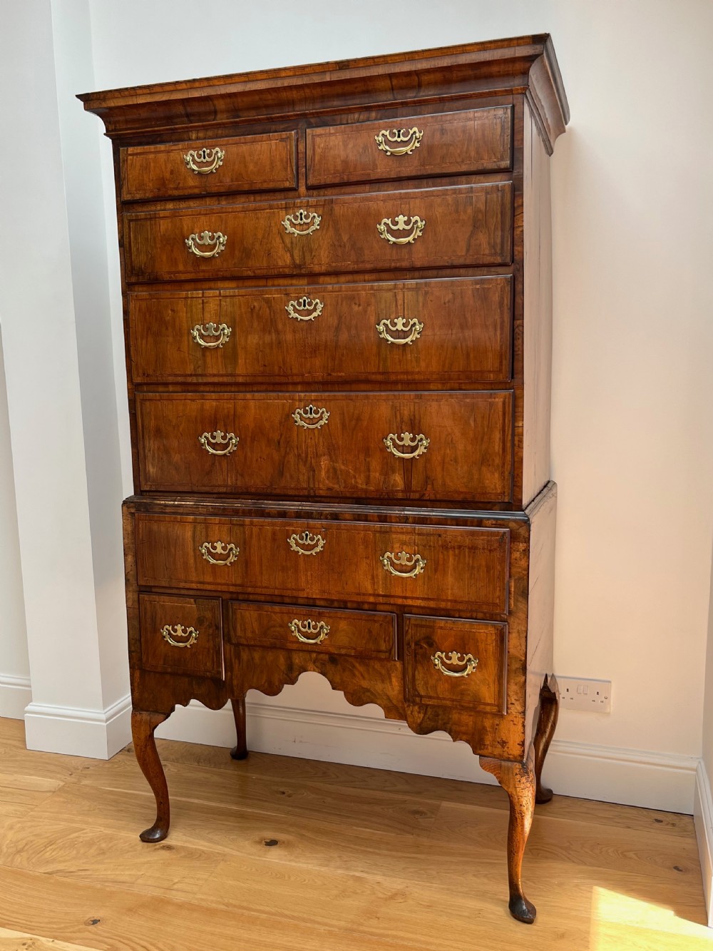 An early 18th-century walnut chest on stand featuring graduated drawers, decorative brass handles, a shaped apron, and four cabriole legs. View II