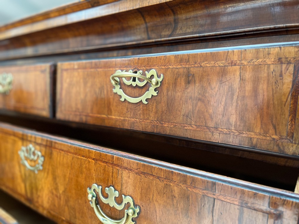 An early 18th-century walnut chest on stand featuring graduated drawers, decorative brass handles, a shaped apron, and four cabriole legs. View IX