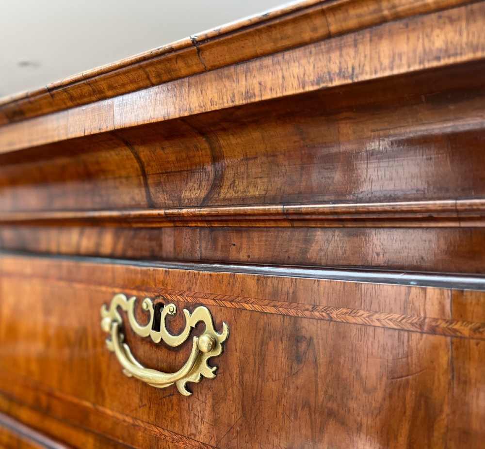 An early 18th-century walnut chest on stand featuring graduated drawers, decorative brass handles, a shaped apron, and four cabriole legs. View XIII