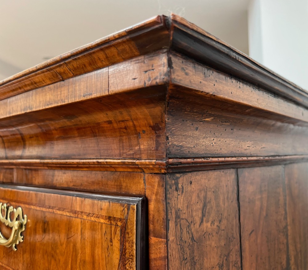 An early 18th-century walnut chest on stand featuring graduated drawers, decorative brass handles, a shaped apron, and four cabriole legs. View XIV