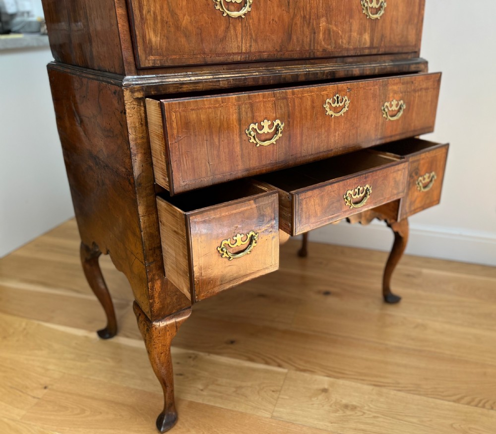 An early 18th-century walnut chest on stand featuring graduated drawers, decorative brass handles, a shaped apron, and four cabriole legs. View XV