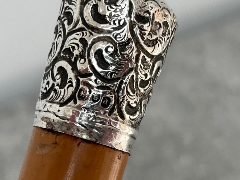 A late Victorian Malacca cane sword stick featuring a silver repousse embossed knop handle and a concealed steel blade alongside its wooden sheath. View V