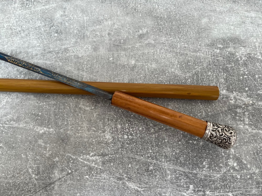 A late Victorian Malacca cane sword stick featuring a silver repousse embossed knop handle and a concealed steel blade alongside its wooden sheath. View X