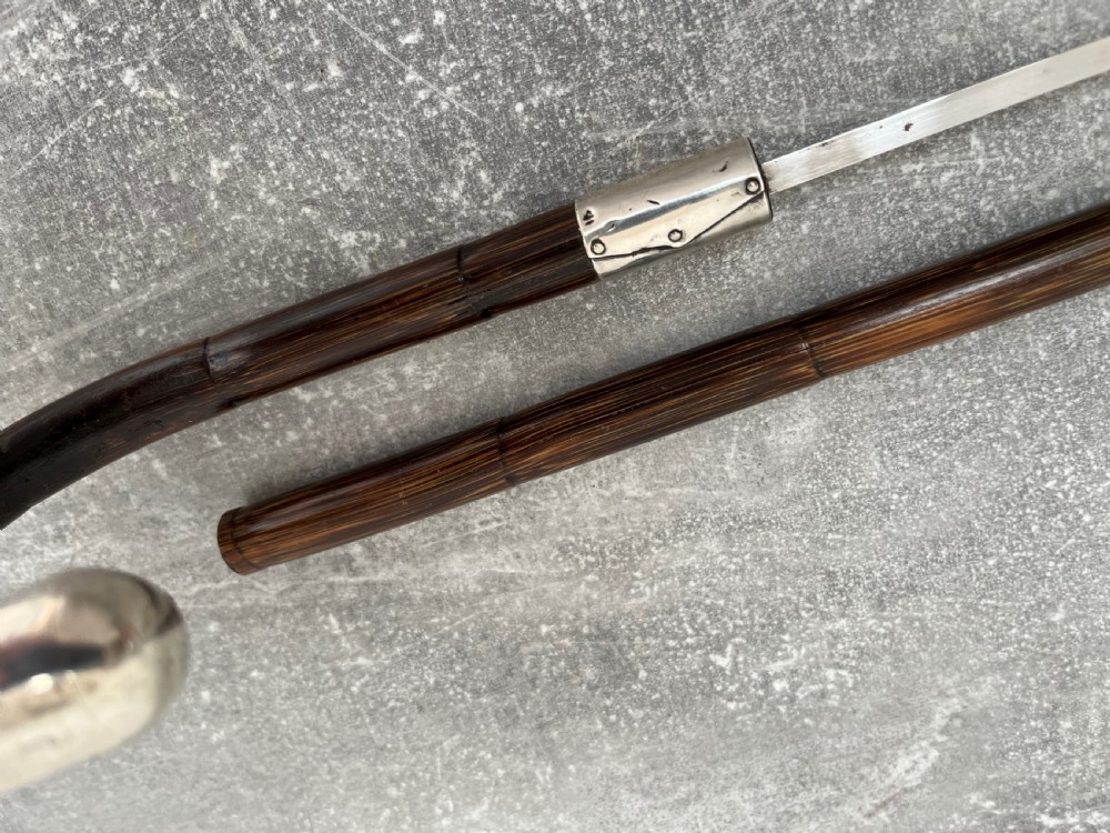 A dark brown malacca cane walking stick featuring a curved crook handle, a silver end cap, a silver collar, and a brass ferrule at the tip. View VII