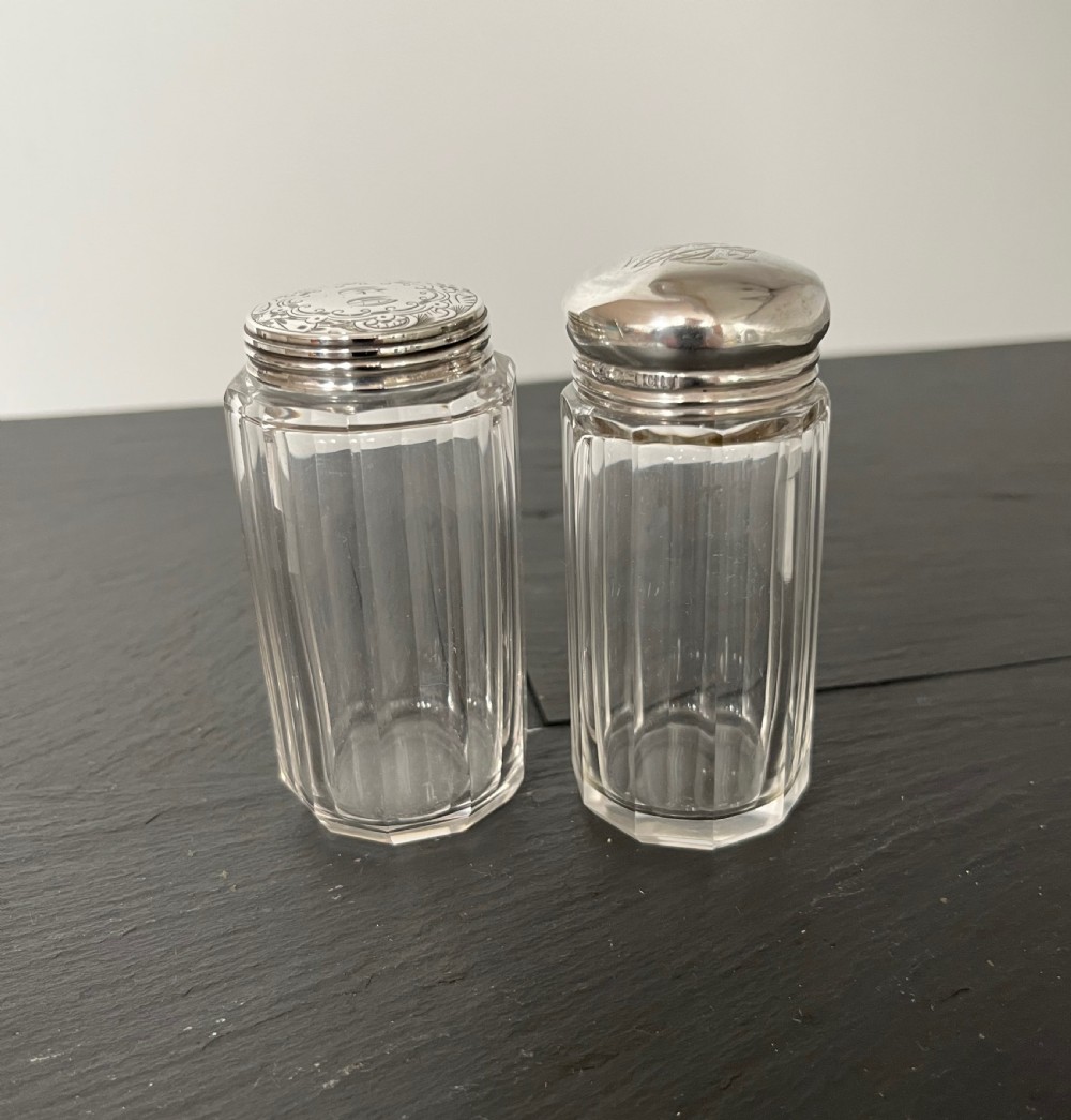 Pair of faceted clear cut glass vanity jars fitted with silver tops featuring engraved and chased detailing. View IX