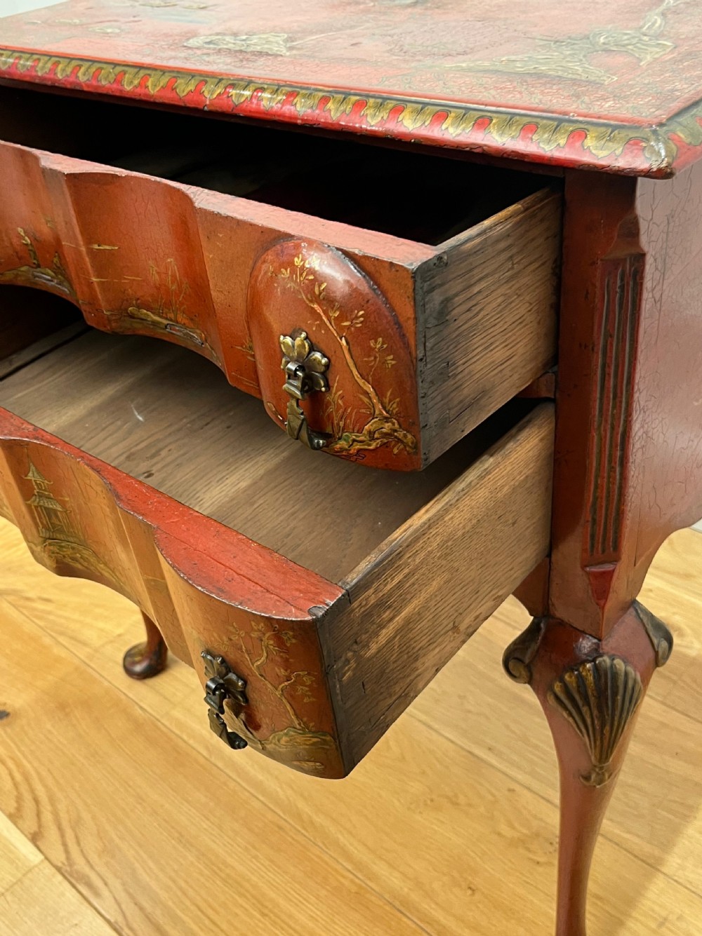A red lacquered side table decorated with hand-painted gilt chinoiserie landscapes, featuring two drawers with brass handles and long cabriole legs. View XII