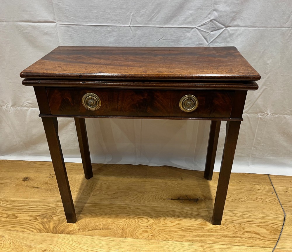 A Regency mahogany fold-over side table featuring tapered square legs, a single drawer with twin circular brass handles, and a hinged timber top.