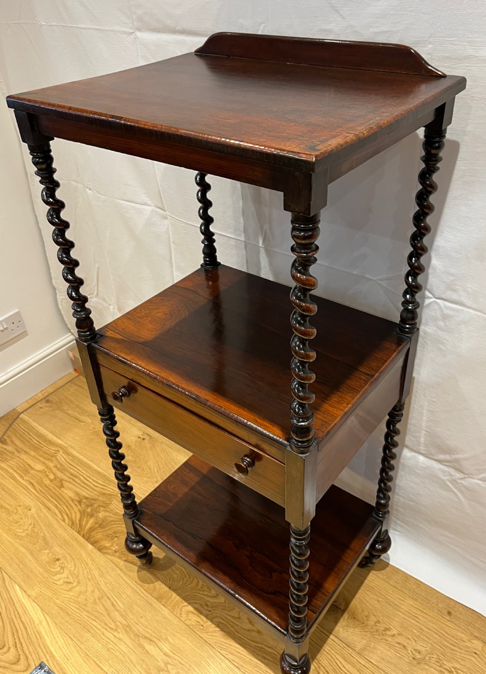 A mid-Victorian dark rosewood whatnot etagere featuring three open tiers, barley twist pillar supports, a central drawer, a gallery back, and turned feet.