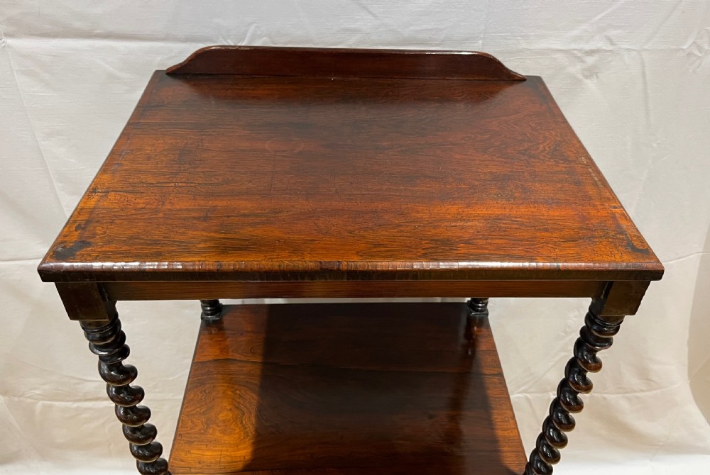 A mid-Victorian dark rosewood whatnot etagere featuring three open tiers, barley twist pillar supports, a central drawer, a gallery back, and turned feet. View II