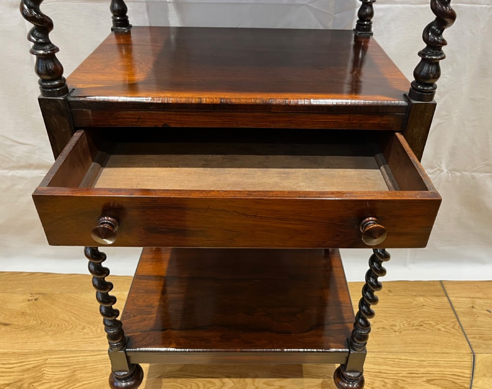 A mid-Victorian dark rosewood whatnot etagere featuring three open tiers, barley twist pillar supports, a central drawer, a gallery back, and turned feet. View IV
