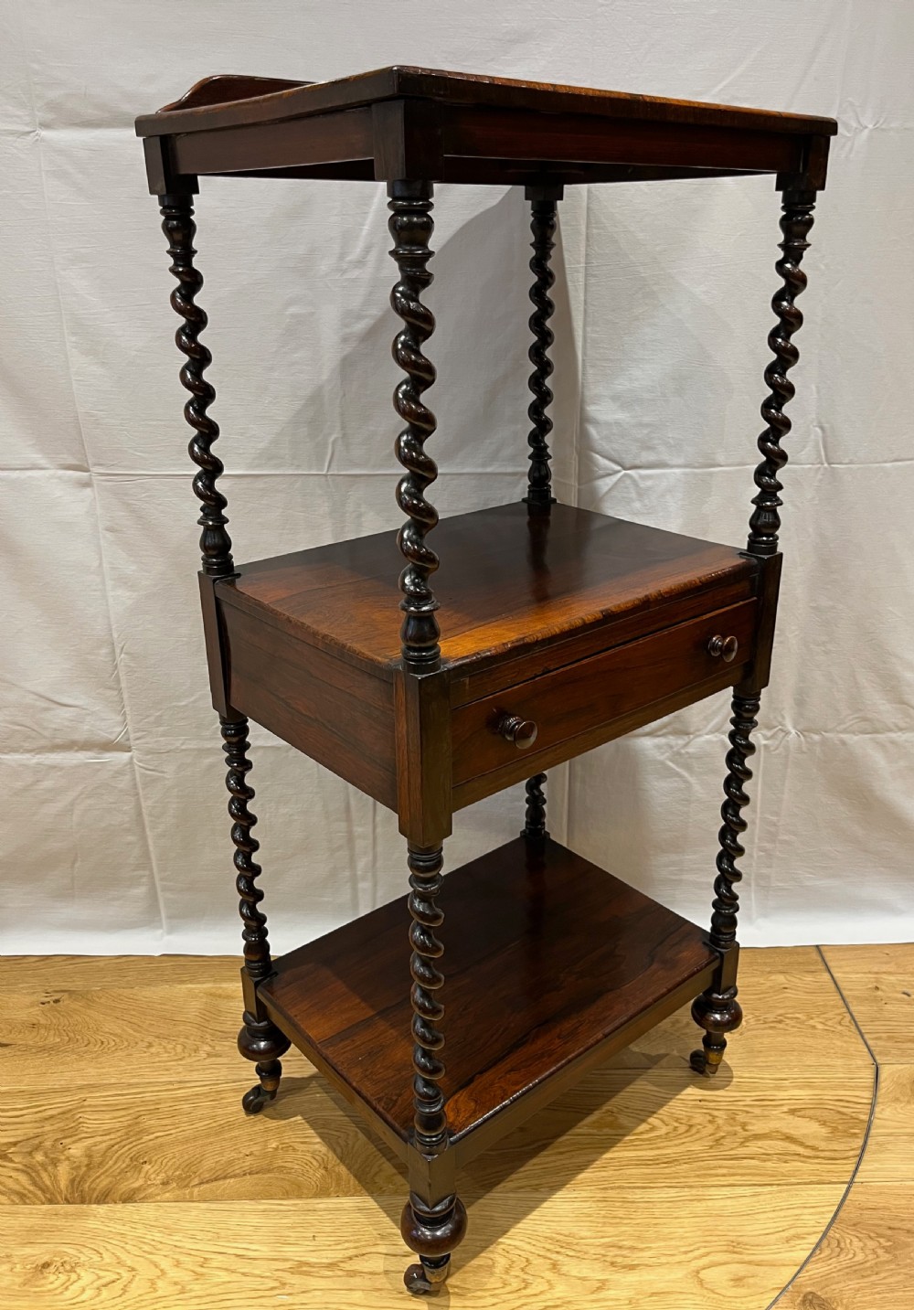 A mid-Victorian dark rosewood whatnot etagere featuring three open tiers, barley twist pillar supports, a central drawer, a gallery back, and turned feet. View V