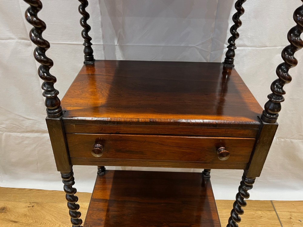 A mid-Victorian dark rosewood whatnot etagere featuring three open tiers, barley twist pillar supports, a central drawer, a gallery back, and turned feet. View VI